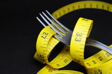 Measuring tape and fork on black background. Diet concept.
