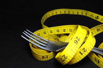 Measuring tape and fork on black background. Diet concept.