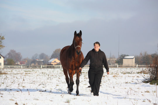 Teenager boy leading bay horse in winter