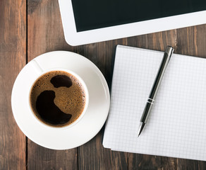 Tablet, paper notebook and coffee on the table
