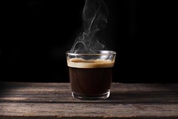 Steaming coffee over wooden surface and black background