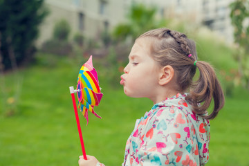 little cute girl blowing pinwheel in nature