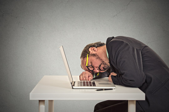 Businessman sleeping on a laptop on grey wall office background 