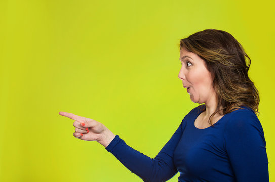 Surprised female pointing out at copy space, green background 