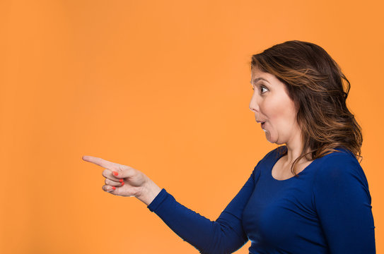 Surprised female pointing out at copy space, orange background 