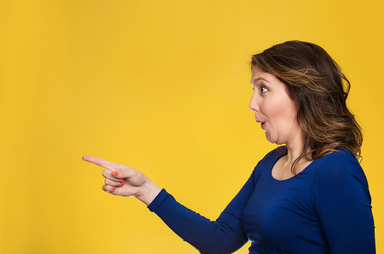 Surprised female pointing out at copy space on yellow background