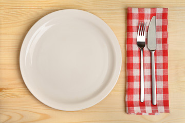 Empty plate with cutlery on red napkin on wooden background.