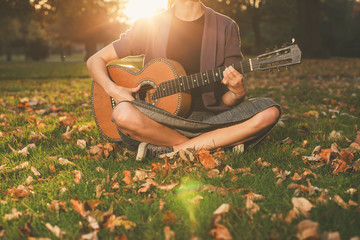Woman playing guitar in park at sunset