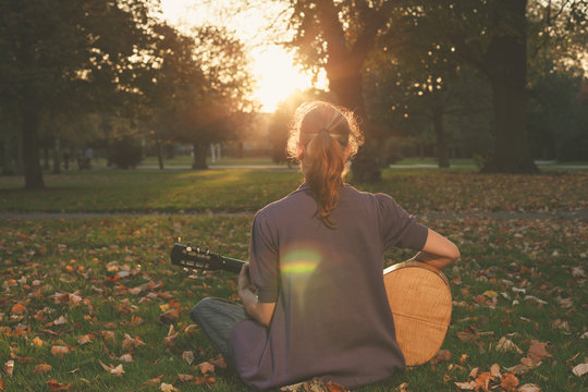 Woman playing guitar at sunset in the park