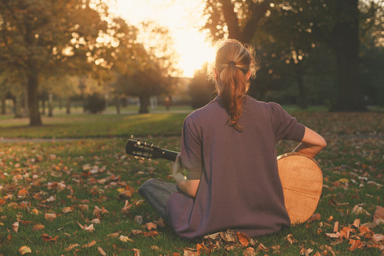 Woman sitting on grass playing guitar at sunset