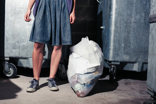 Woman standing next to bins with a bag of rubbish