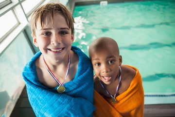 Little boys standing by the pool in towels with medals