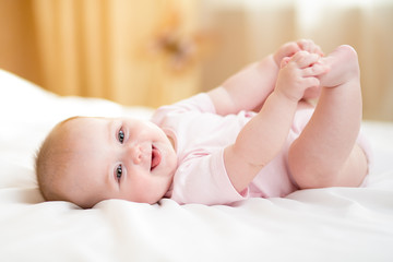 baby girl lying on white bed and holding her legs