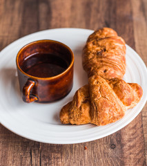 croissant with chocolate on a white plate and coffee, breakfast