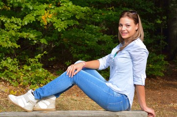 Obraz premium Beautiful young girl sitting on the bank in park
