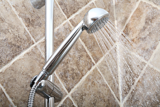 Silver shower head with running water in bathroom