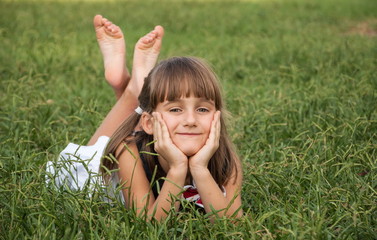 Cute little girl lies on a lawn in park and smiling
