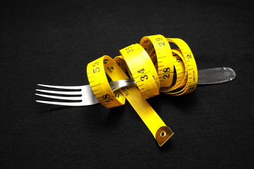 Measuring tape and fork on black background. Diet concept.