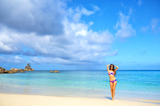 Beautiful young female in bikini standing on tropical beach