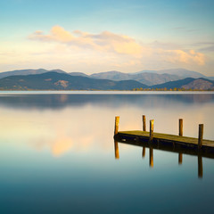 Wooden pier or jetty and on a blue lake sunset and sky reflectio