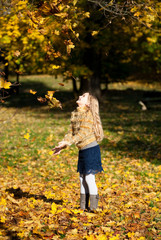 A pretty blond girl throwing up the tree leaves