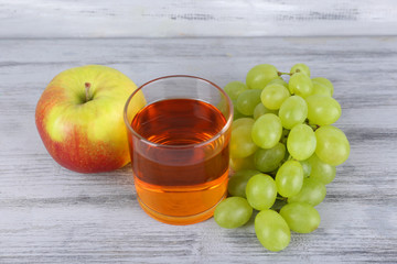 glass of juice with fresh grape and apple on grey wooden table