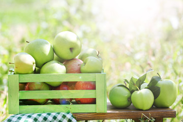 Juicy apples in wooden box on grass, outdoors