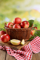 Sweet apples in wooden basket on table on bright background