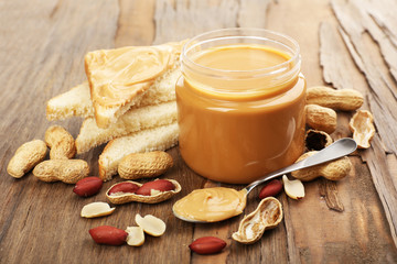Creamy peanut butter in jar, on wooden table