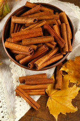 Cinnamon sticks in bowl with yellow leaves on wooden background