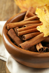 Cinnamon sticks in bowl with yellow leaves on wooden background
