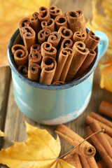 Cinnamon sticks in mug with yellow leaves on wooden background