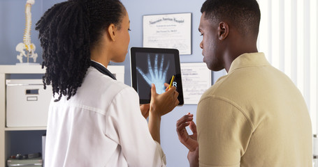 Black female doctor sharing hand x ray with patient on tablet