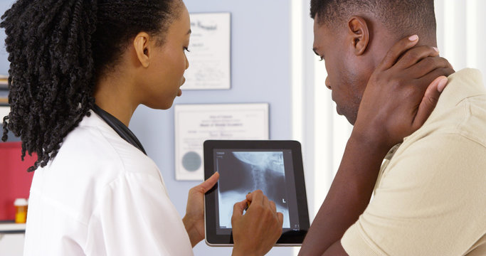 Patient With Neck Pain Talking To Female Doctor About X Ray On Tablet