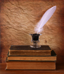low key image of white Feather, inkwell and ancient books on old