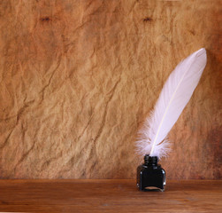 low key image of white Feather and inkwell on old wooden table