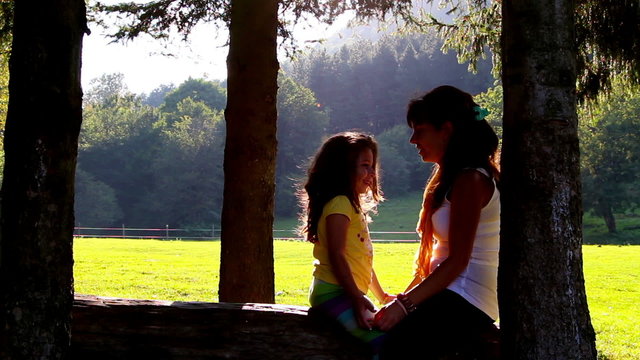 Mother and daughter hugging and kissing on tree log in Sunset