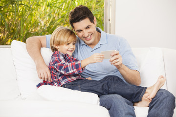 Fototapeta premium Vater und Sohn auf dem Sofa, machen Selfies