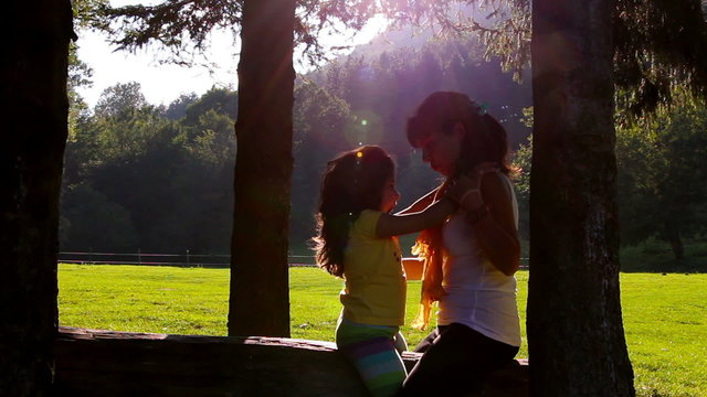 Mother and daughter hugging and kissing on tree log in Sunset