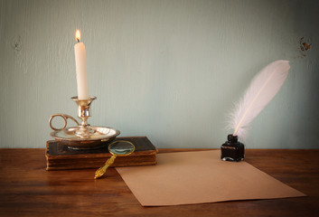 low key image of white Feather, inkwell, burning Candle and anci