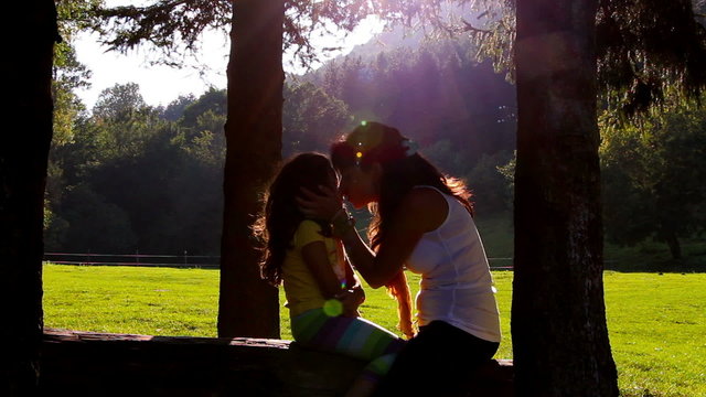 Mother and daughter hugging and kissing on tree log in Sunset
