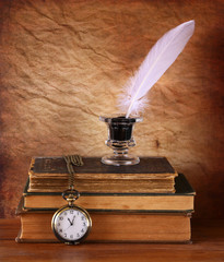 low key image of white Feather, inkwell and ancient books on old