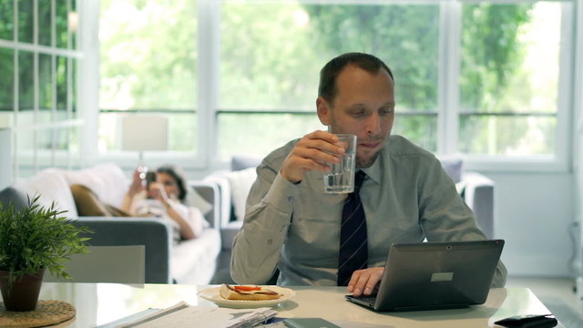 Businessman drinking water and working on laptop at home