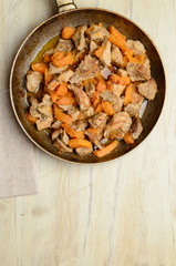Fried pieces of meat and pumpkin in a pan on a wooden table