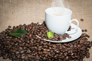 cup of coffee with a smoke and roasted coffee beans on burlap.