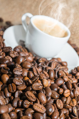 cup of coffee with a smoke and roasted coffee beans on burlap