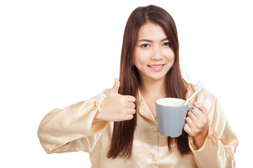 Asian woman in pajamas thumbs up with toothbrush in mug