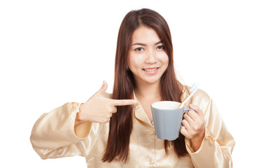 Asian woman in pajamas point to toothbrush in mug