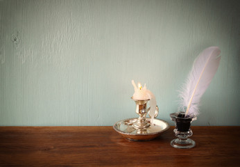 low key image of white Feather, inkwell, and candle on old woode