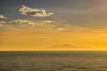 Naklejka na ściany i meble Sailing boats at sunrise against a silhouetted isle of Elba